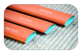 Three lengths of red-orange heat-shrink sleeve printed GVOT 50/25, laid on a galvanised sheet with a pale turquoise liner visible in each bore.